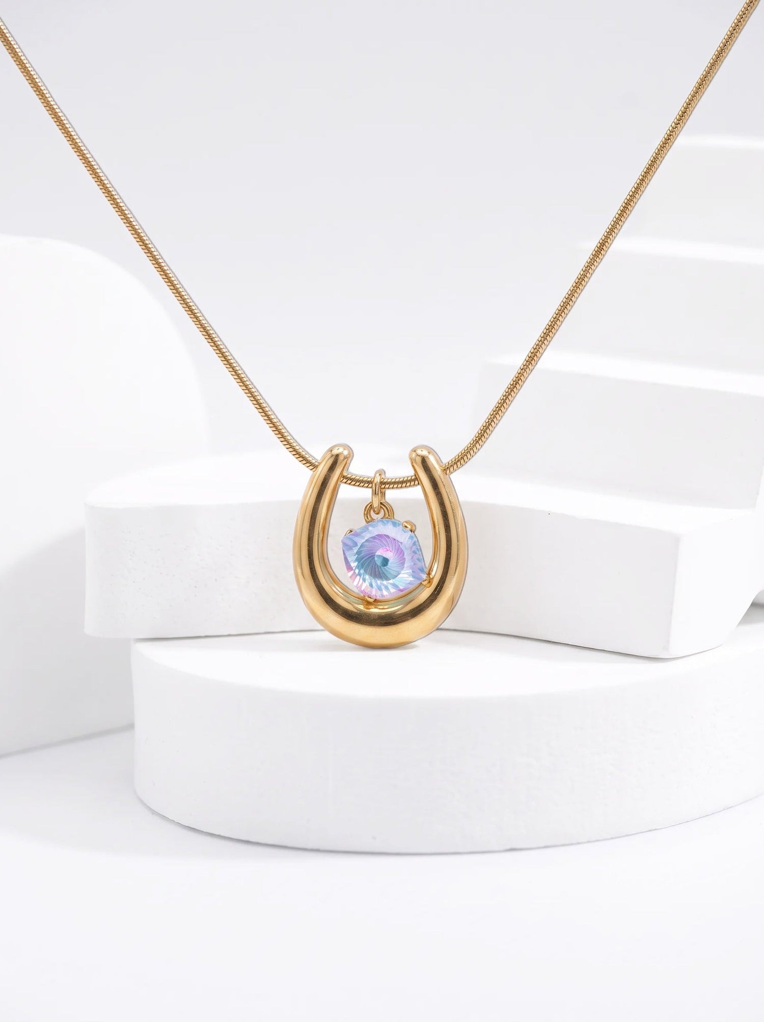 Close-up of a gold-tone horseshoe necklace featuring an iridescent blue-violet spiral-cut zircon pendant.