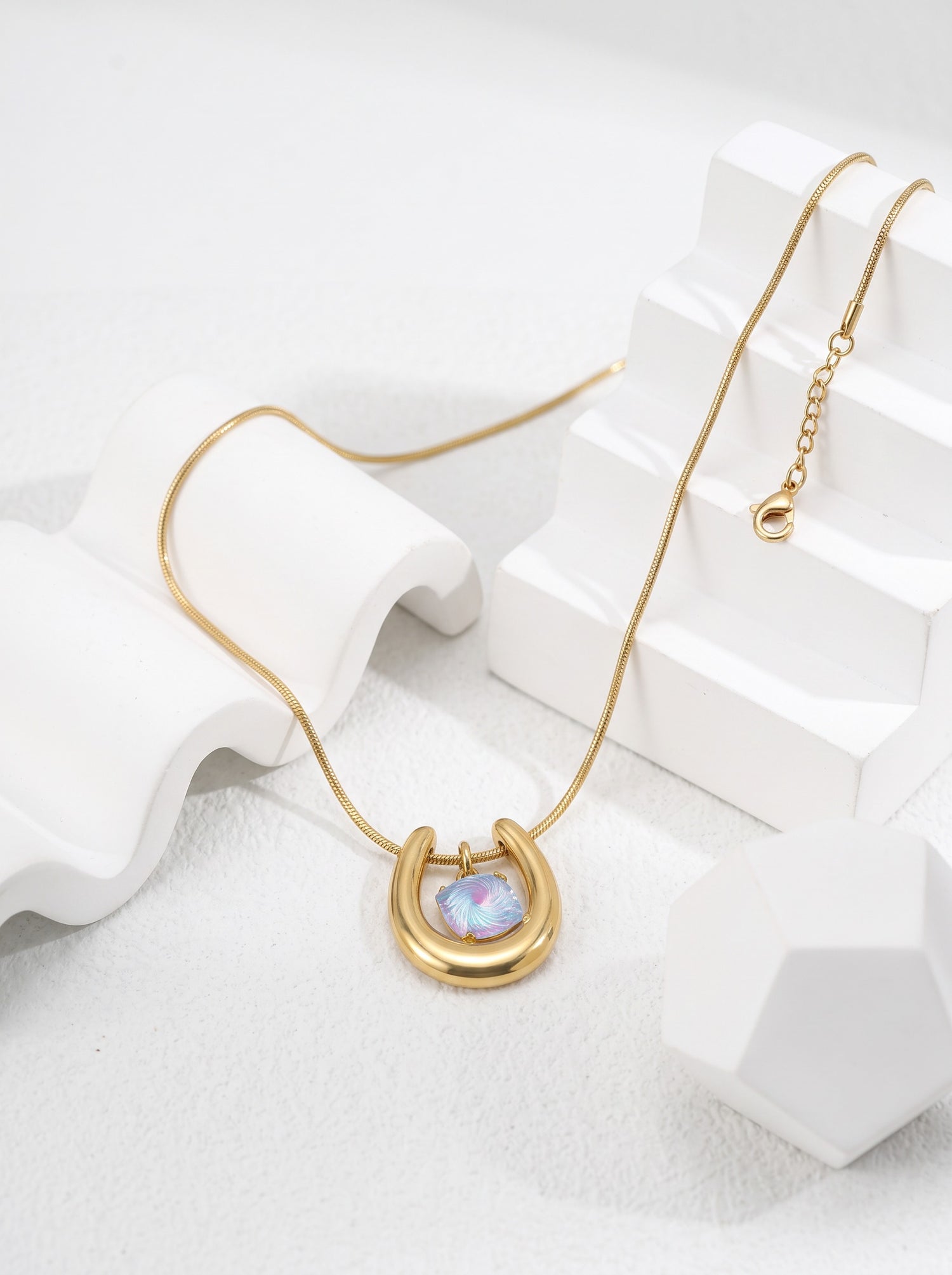 Close-up of a gold-tone horseshoe necklace featuring an iridescent blue-violet spiral-cut zircon pendant.