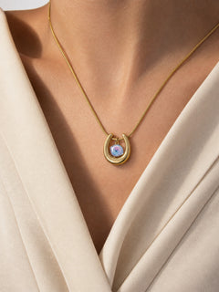Close-up of a gold-tone horseshoe necklace featuring an iridescent blue-violet spiral-cut zircon pendant.