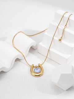 Close-up of a gold-tone horseshoe necklace featuring an iridescent blue-violet spiral-cut zircon pendant.